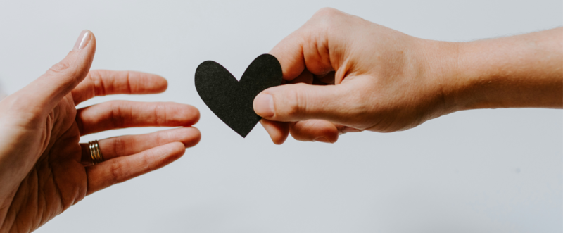Mano che porge un cuore nero ad un'altra mano.