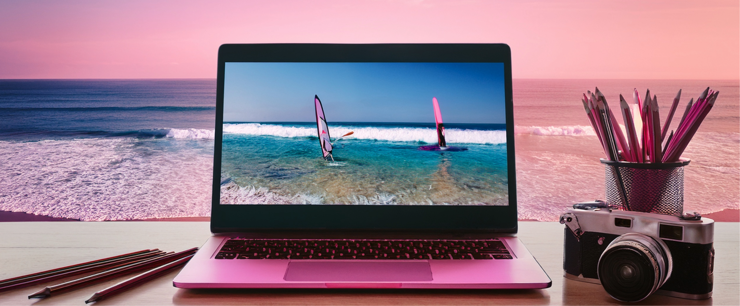 immagine di un tavolo vista mare con sopra un pc, una macchina fotografia e delle matite 
