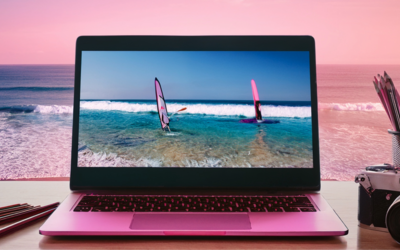 immagine di un tavolo vista mare con sopra un pc, una macchina fotografia e delle matite 