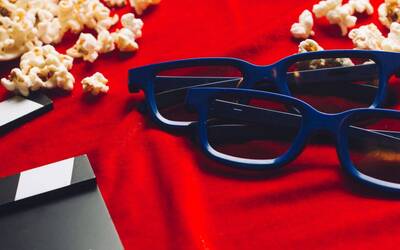 Occhiali per film in 3D, popcorn e strumento da regista su sfondo rosso.