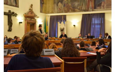 ragazzi e ragazze seduti all'interno dell'aula del consiglio comunale ascoltano un adulto che parla