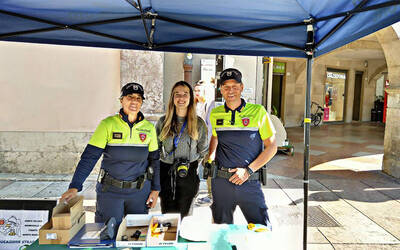 una ragazza con al collo una macchina fotografica e due agenti della polizia locale sorridono al fotografo presso lo stand della Polizia locale