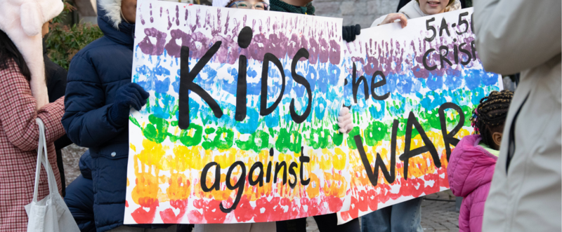 Uno striscione con i colori dell'arcobaleno sorretto da dei bambini in piazza