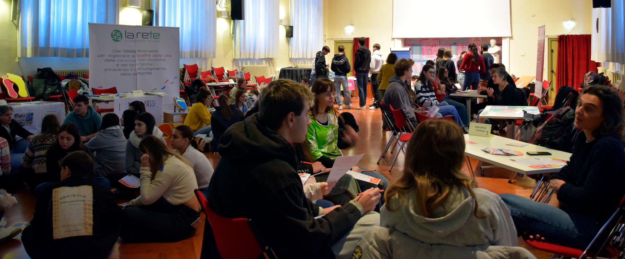 Ragazzi e ragazze a gruppi che parlano con operatori di associazioni in una palestra