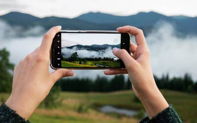 Mani che sorreggono uno smartphone mentre fotografano un paesaggio.