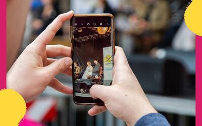 Mani che reggono un cellulare che fotografa persone che dibattono.