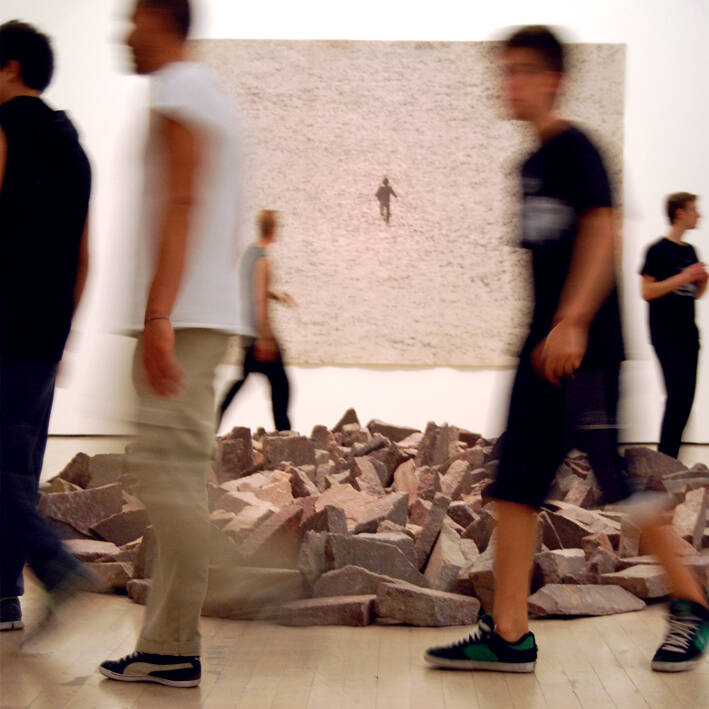 cinque ragazzi camminano intorno ad un'installazione artistica costituita da pietre deposte per terra