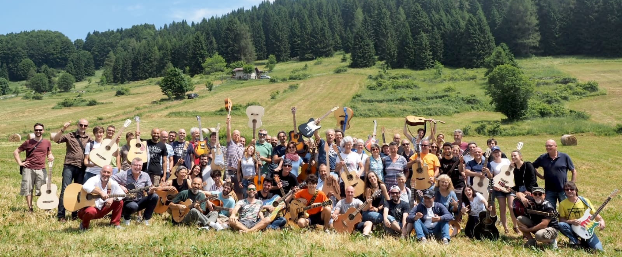 Un gruppo numeroso di persone con lo sfondo di un prato e dei boschi