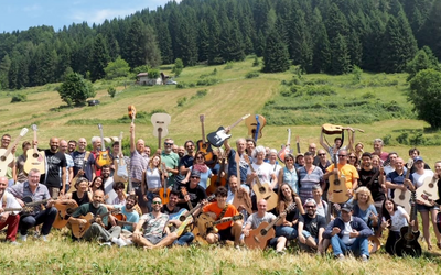 Un gruppo numeroso di persone con lo sfondo di un prato e dei boschi