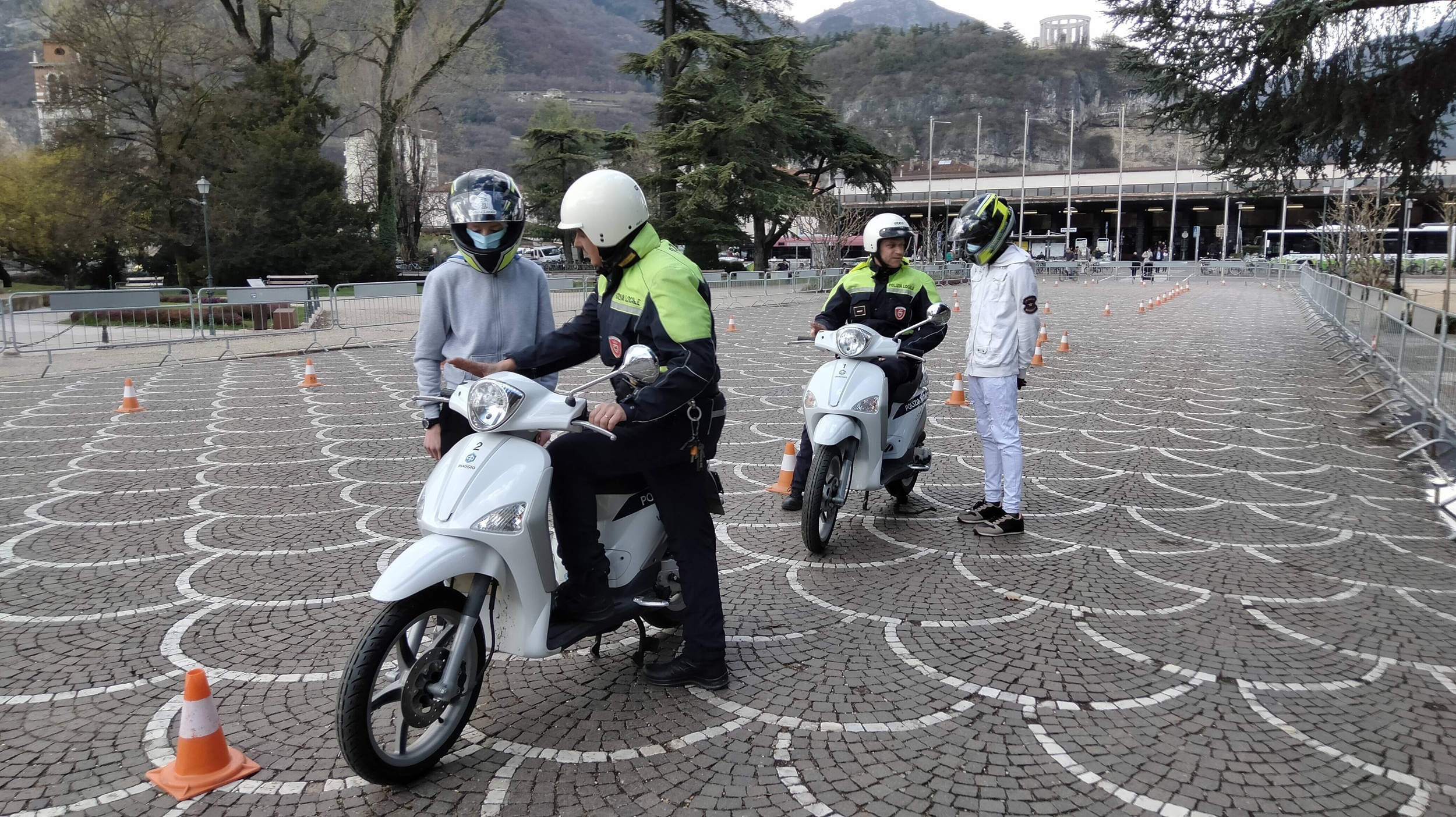 in sosta, due agenti di polizia locale mostrano a due ragazzi i comandi del motorino