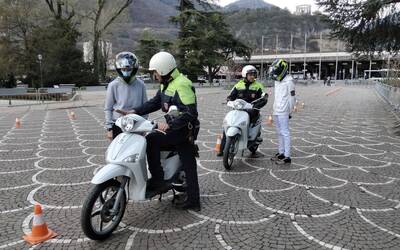 in sosta, due agenti di polizia locale mostrano a due ragazzi i comandi del motorino