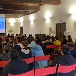 Sessanta giovani seduti in una sala che ascoltano un adulto che parla