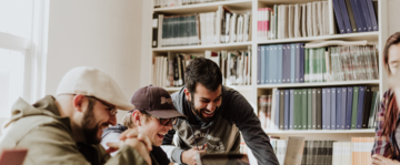 tre ragazzi ad un tavolo con dei pc e sullo sfondo una libreria 