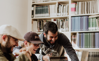 tre ragazzi ad un tavolo con dei pc e sullo sfondo una libreria 