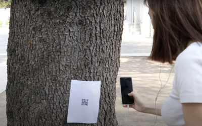 Un foglietto con QR code appeso su un albero viene inquadrato con uno smartphone da una ragazza