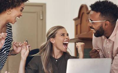 Due ragazze e un ragazzo esultano contenti davanti ad un computer