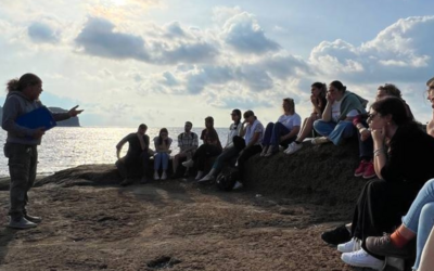 giovani sull'isola di Ventotene ascoltano la storia del Carcere di S. Stefano guardandolo dalla spiaggia