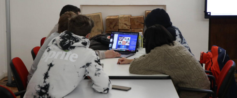 Cinque ragazzi e ragazze seduti su un tavolo attorno ad un computer portatile