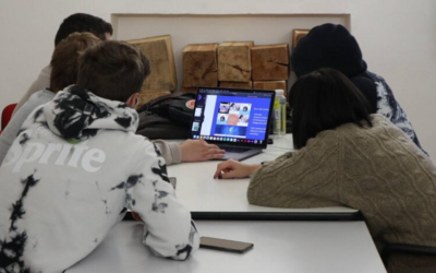 Cinque ragazzi e ragazze seduti su un tavolo attorno ad un computer portatile