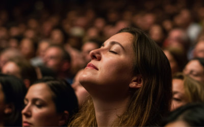 varie persone in un teatro, una donna in primo piano con il viso rivolto verso l'alto sembra in ascolto